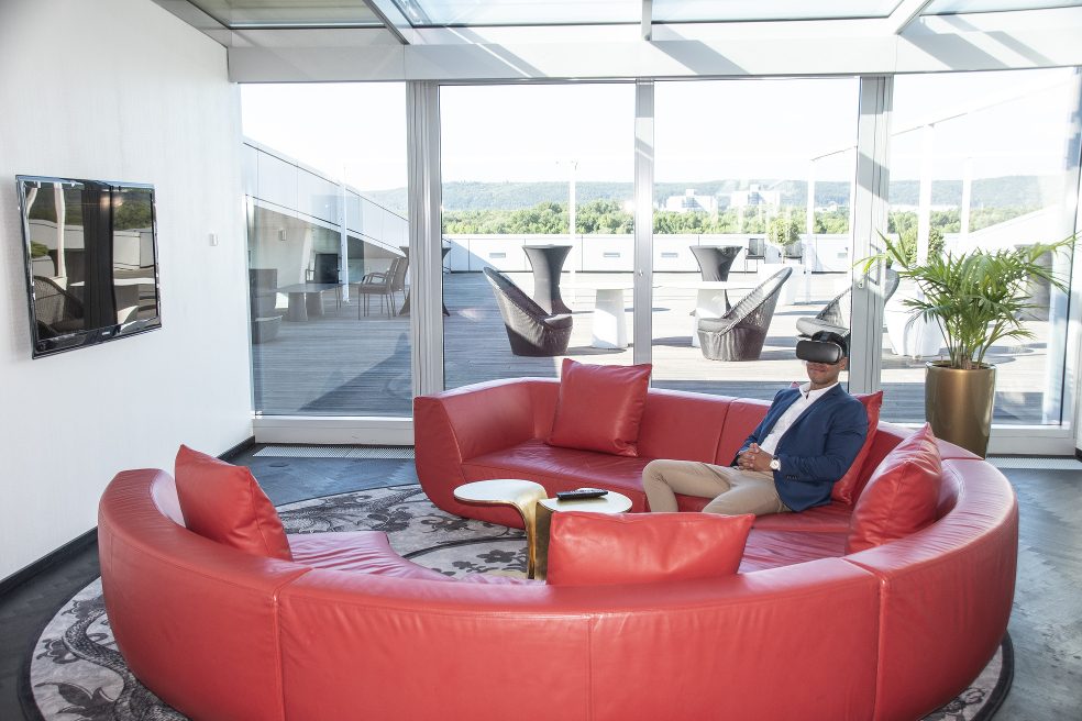 Ein Gast mit VR-Brille auf dem roten Sofa im Kameha Grand