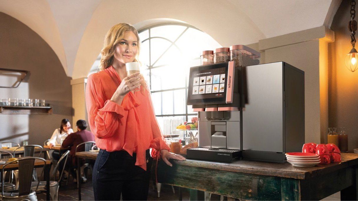 Eine Frau mit einer Tasse vor einer Kaffeemaschine von Schaerer
