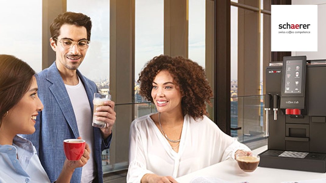 Drei Menschen trinken Kaffee an einer Schaerer-Kaffeemaschine